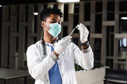 African doctor in a medical mask prepares to inject coronavirus covid-19 vaccine. Black doctor in white medical robe with syringe for making vaccination