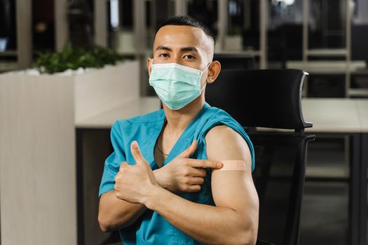 Handsome asian man vaccinated against coronavarus and showing patch on his arm. Covid-19 vaccination. Filipino man in medical mask.