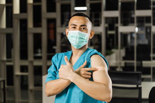 Handsome asian man vaccinated against coronavarus and showing patch on his arm. Covid-19 vaccination. Filipino man in medical mask.