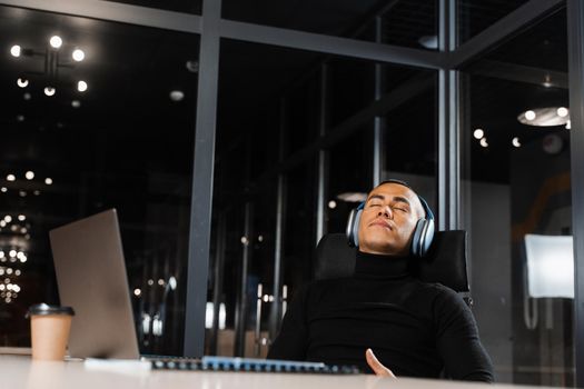 Overtime working. Asian man with closed eyes is resting at work at laptop. Tired male programmer taking a break due to overtime work.