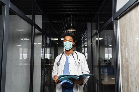 Black medical student reads books and prepares for an exam. African in a medical robe and mask looks at the notes