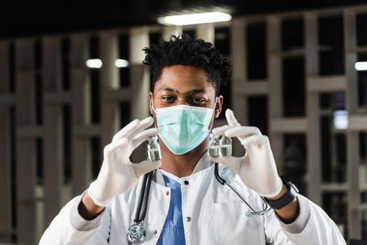 Black doctor with 3 doses of vaccine. Booster vaccination. African doctor in medical mask is holding vaccines in hand