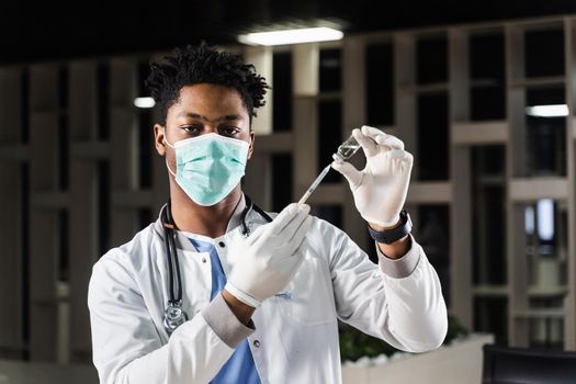 African doctor in a medical mask prepares to inject coronavirus covid-19 vaccine. Black doctor in white medical robe with syringe for making vaccination