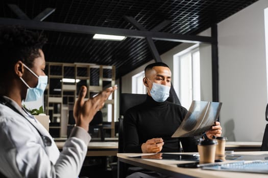 Asian patient is consulting a black surgeon doctor and discussing x-ray picture. Preparation for the operation. African doctor examining a patient