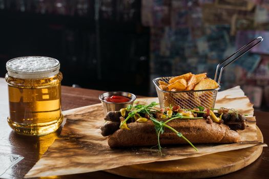 Barbecue grilled hot dog and beer with yellow mustard and ketchup on wooden background. Hot dog sandwich with potato fries and sauces.