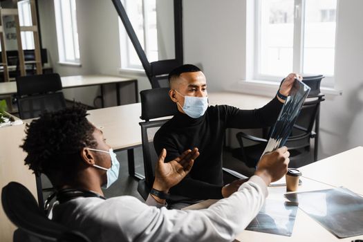 Asian patient is consulting a black surgeon doctor and discussing x-ray picture. Preparation for the operation. African doctor examining a patient