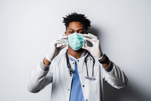 Handsome African doctor with coronavirus covid-19 vaccine. Black doctor in medical mask is holding vaccine on white background