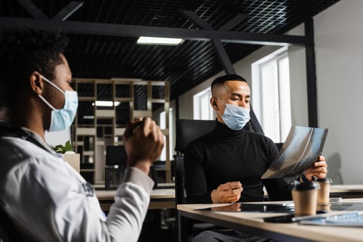 Asian patient is consulting a black surgeon doctor and discussing x-ray picture. Preparation for the operation. African doctor examining a patient