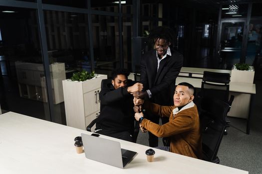 Multiethnical diverse teamwork online with laptop. African and Asian colleagues making hand stack of fists. Community spirit and friendship. Keeping high motivation