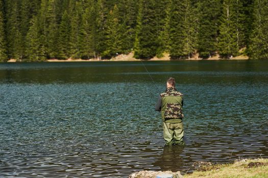 Fisher man stands in the water and catch fish in the lake on a background of mountains. High quality photo