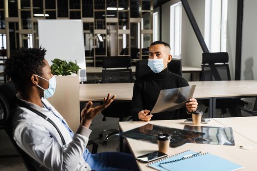 Handsome asian patient with x-ray image of fracture of foot bones at black doctor consultation. African surgeon discussing x-ray with patient