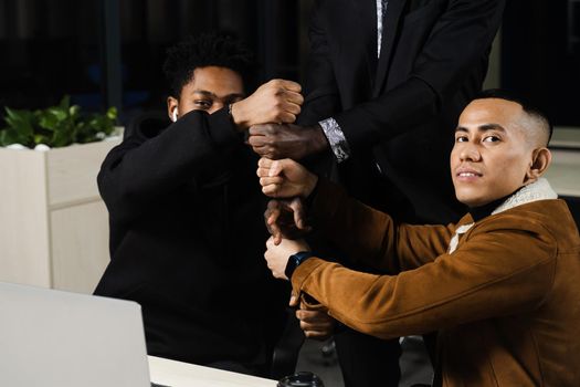 Multiethnical diverse colleagues making hand stack of fists. Black africans and asian working online with laptop in office