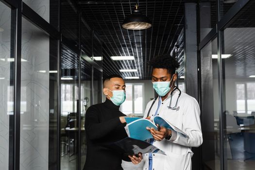 Asian patient with x-rays asks an African doctor about treatment of pneumonia and pleurisy. Black surgeon consult and help Asian man