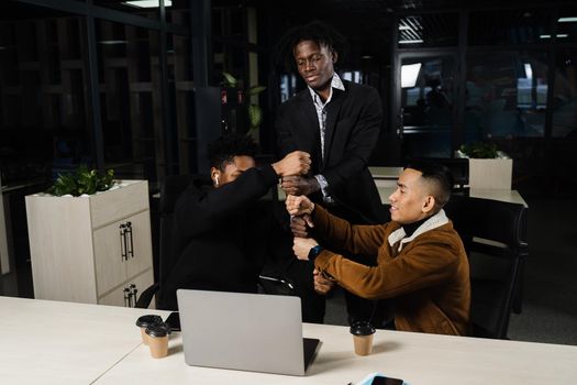 Multiethnical diverse colleagues making hand stack of fists. Black africans and asian working online with laptop in office