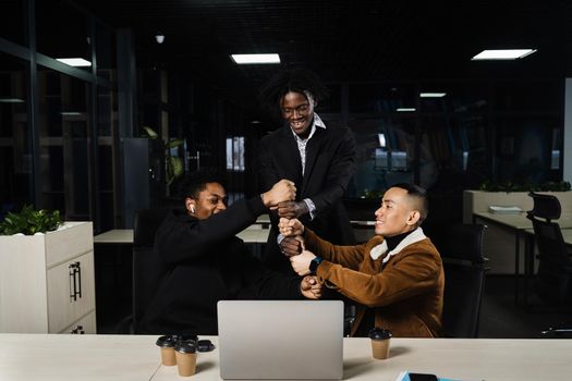 African and Asian colleagues making hand stack of fists. Multiethnical diverse teamwork online with laptop. Community spirit and friendship. Keeping high motivation