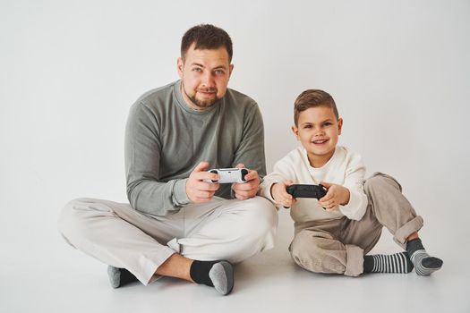Emotional family playing console games on a white background. Father and son play gamepad games together