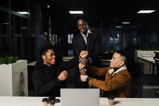 Multiethnical diverse colleagues making hand stack of fists. Black africans and asian working online with laptop in office.