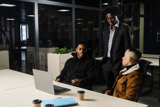 Multiethnic group of African and Asian colleagues are working on laptop on business project. Two black handsome managers teamwork with an Asian man and create creative ideas