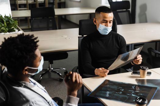 Asian patient is consulting a black surgeon doctor and discussing x-ray picture. Preparation for the operation. African doctor examining a patient