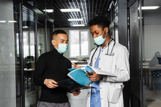 Discussion and consultation between black doctor and patient in medical clinic. African surgeon treats Asian handsome man