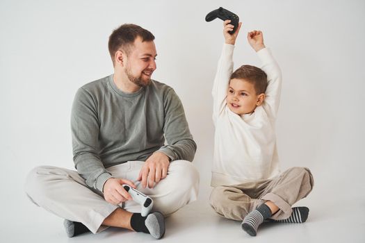 Son won father in game on console. Happy child with gamepad raises his hands up and rejoices in the victory in the game