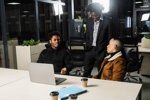 Multiethnic group of African and Asian colleagues are working on laptop on business project. Two black handsome managers teamwork with an Asian man and create creative ideas