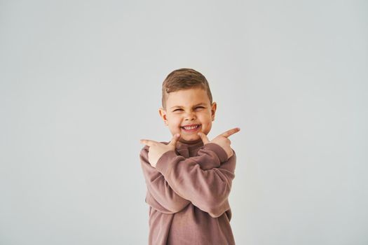 Happy handsome child boy smiling and points his fingers up for choose. Business advertising for children stores and shops