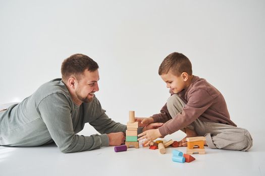 Dad and son smiling, having fun and playing colored bricks toy on white background. Paternity. Caring father with his child