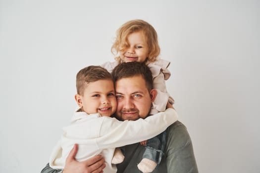 Close-up portrait of father, son and daughter. Happy family hugging and smiling on white background. Paternity. Single father bring up his children