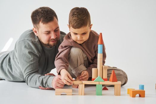 Paternity. Son and dad playing with colored bricks toy on white background. Father takes care of his kid