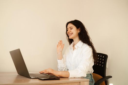 Positive caucasian girl enjoying friendly video call on laptop computer using web camera for communicating. Young woman waves her hand and greets her friends by video call