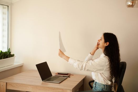 Applicant with laptop holds papers with exam results in his hands and rejoices. Student girl passed exam and rejoices at high mark. Online education and distance learning