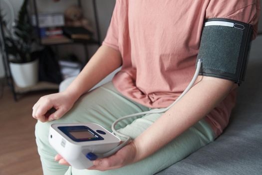 Selective focus girl is taking care for health with hearth beat monitor and blood pressure and heart rate monitor with digital pressure gauge. Health care and Medical concept. The topic of high blood pressure is hypertension disease. Close-up macro young caucasian woman hands using automatic tonometer to check pressure at home in bedroom on bed.