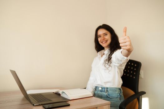 Girl student showing thumbs up. Schoolgirl with laptop done homework online and gesturing thumbs up at table at home