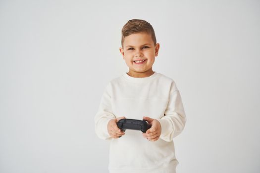 Youngster with gamepad smiling and play game on white background. Gamer child playing games