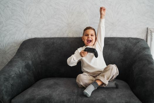 Emotional child with a gamepad rejoices, shouts and raises his hands up because he won the game. Happy boy play games at home