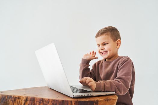 Emotional child with laptop talking with friends online. Handsome kid typing text on laptop and smile