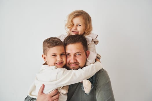 Close-up portrait of father, son and daughter. Happy family hugging and smiling on white background. Paternity. Single father bring up his children