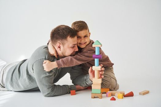 The son hugs his caring father on a white background. Father and child play colored wooden blocks toy. Fatherhood