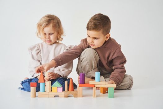 Boy and baby girl smiling, having fun and playing colored bricks toy on white background. Children have smiling and have fun together