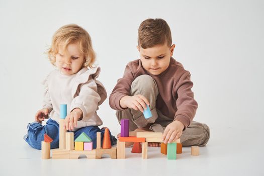 Boy and baby girl smiling, having fun and playing colored bricks toy on white background. Children have smiling and have fun together