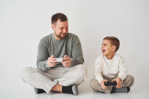 Emotional family playing console games on a white background. Father and son play gamepad games together