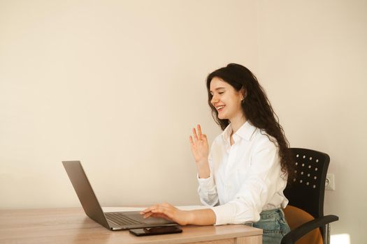 Positive caucasian girl enjoying friendly video call on laptop computer using web camera for communicating. Young woman waves her hand and greets her friends by video call