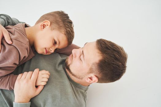 The son lies on the shoulder of his father. Dad hugs his child and smiles. Child care