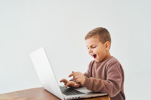 Emotional child play online games on laptop. Gambling addiction. Handsome kid gamer is gaming on laptop on white background