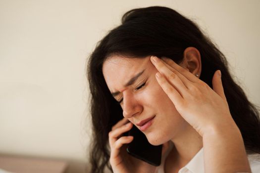 Headache. Close-up of exhausted overstressed girl and talking on the phone. Portrait of attractive young woman feeling sick and having headache