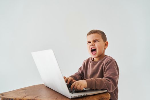 Emotional child with laptop shout. Gambling addiction. Handsome child gamer play online games on laptop on white background