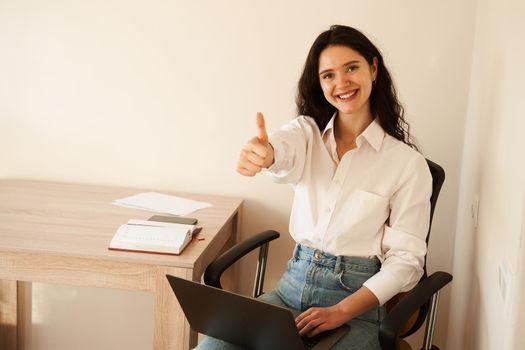 Girl showing thumbs up and smiling. Student studying online using laptop on lap at home. Online education and distance learning