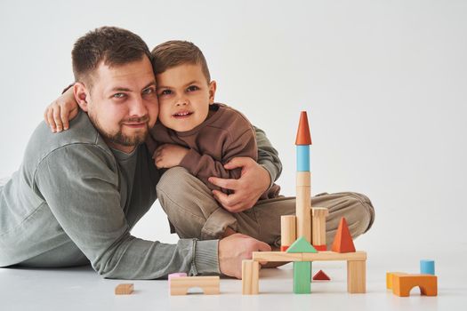 Paternity. Son and dad playing with colored bricks toy on white background. Father takes care of his kid