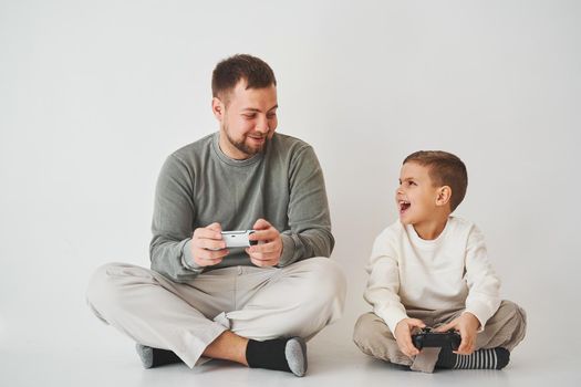 Emotional family playing console games on a white background. Father and son play gamepad games together